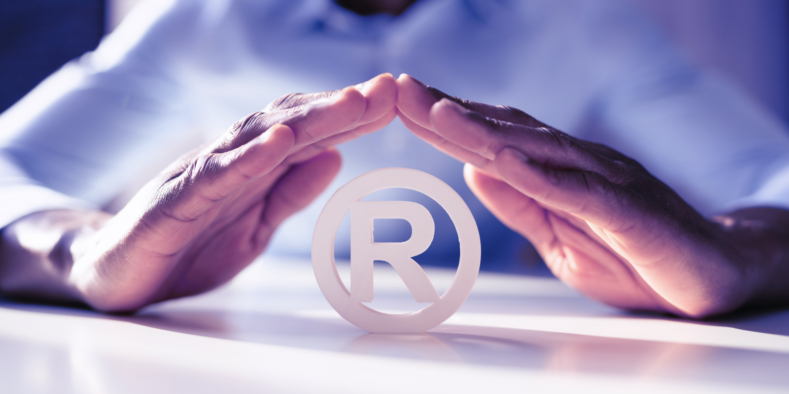 Mãos protegendo símbolo de marca registrada, representando a importância do registro de marca e da proteção legal para empresas.